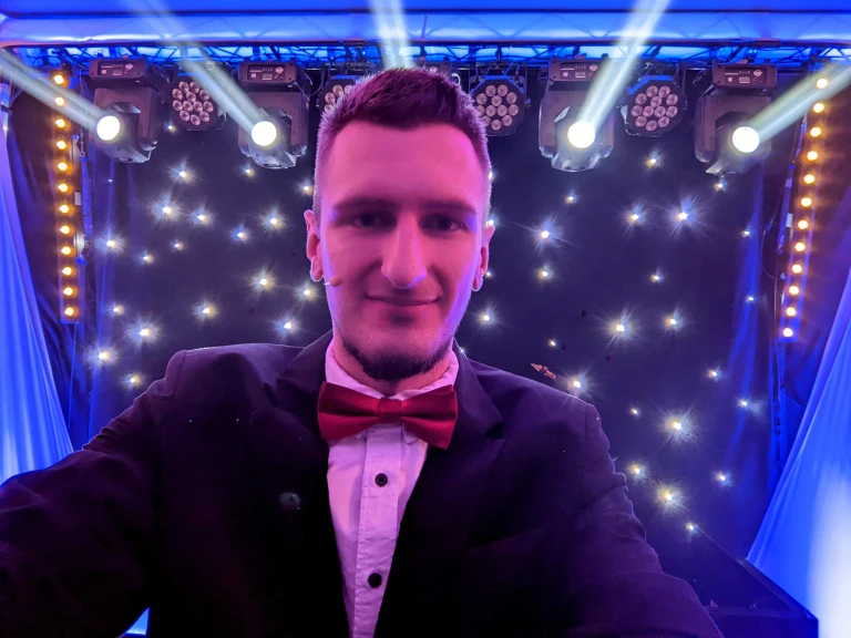 Iluzjonista Konrad Mościński na tle profesjonalnego oświetlenia scenicznego z ruchomymi głowami i kurtyną LED