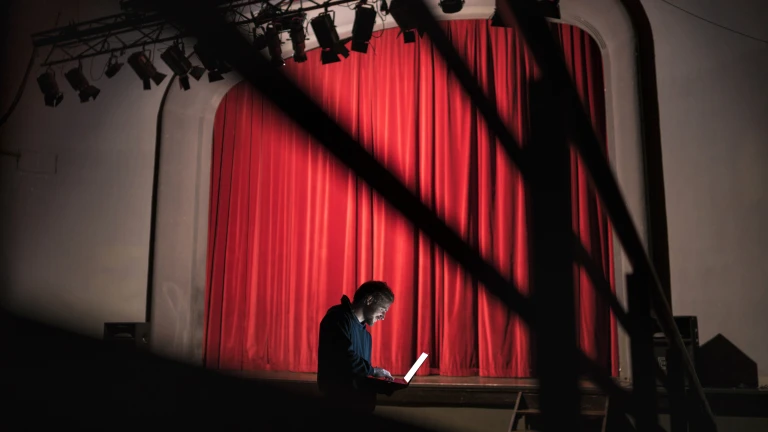 Sylwetka mężczyzny z laptopem na tle czerwonej kurtyny teatralnej