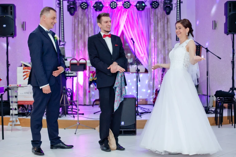 Iluzjonista Konrad Mościński podczas interaktywnego triku z Parą Młodą. Wszyscy są roześmiani i uśmiechnięci za sprawą komediowego dialogu.